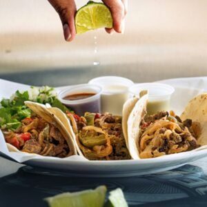 a plate of tacos with a lime being drizzled on top